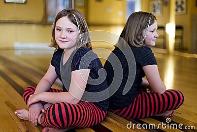 Little girl in casual clothes sitting cross-legged on the floor of a danse studio Stock Photo