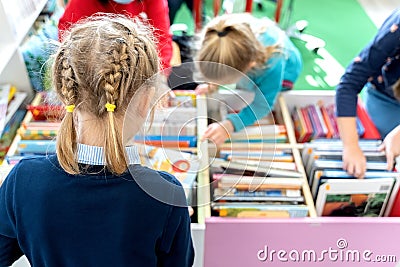 Little girl chooses, takes book with fairy tales from box in children`s library.Special reading kids room.Many shelves with brigh Editorial Stock Photo