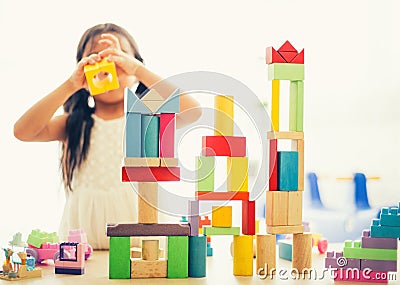 little girl in a colorful shirt playing with construction toy blocks building a tower . Kids playing. Children at day care. Child Stock Photo