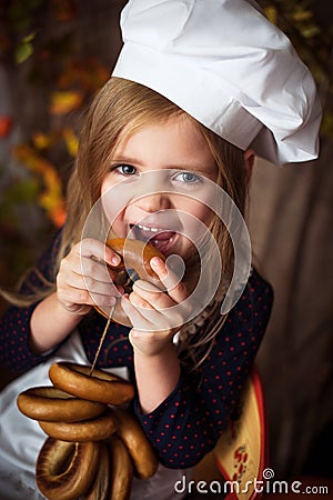 Little girl in cook clothes with bagels in her hands and smiling Stock Photo