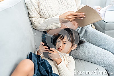 Little girl is cute lying next to the cell phone playing Pregnant Asian single mom Sit comfortably on the sofa in the living room Stock Photo
