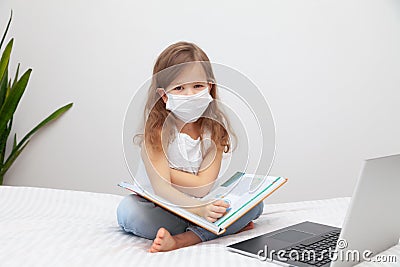 Little girl in disposal medical mask doing homework with laptop Stock Photo