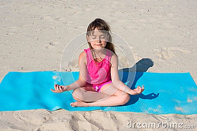 Little girl does yoga on the beach. The concept of sport and active play in the summer. Beach gymnastics Stock Photo