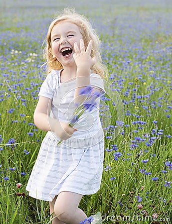 A little girl in a dress and with a bouquet of flowers laughs and plays in a field with cornflowers on a summer day Stock Photo