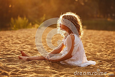 Little girl in dress sitting on the sand Stock Photo