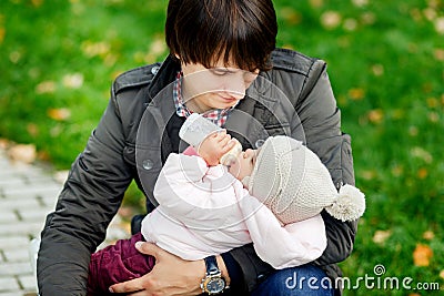 Little girl drinking from bottle on hands father in park Stock Photo