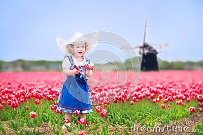 Little girl in Dutch costume in tulips field with windmill Stock Photo