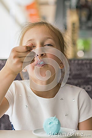 Little girl eating blue ice cream in a cafe. Girl delighted with ice cream. Adorable little girl eating ice cream at summer. Stock Photo