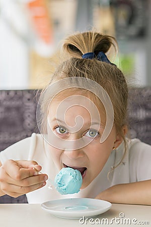 Little girl eating blue ice cream in a cafe. Girl delighted with ice cream. Adorable little girl eating ice cream at summer. Stock Photo