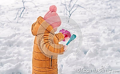 A Little Girl enjoys playing In The Snow. A three-year-old girl in warm clothes plays outdoors in the winter season. Family winte Stock Photo