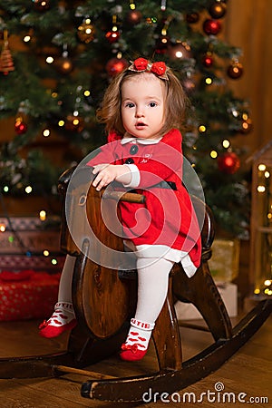 Little girl in a festive red dress on a wooden swing rocking horse. Christmas parties are a fabulous time for children Stock Photo