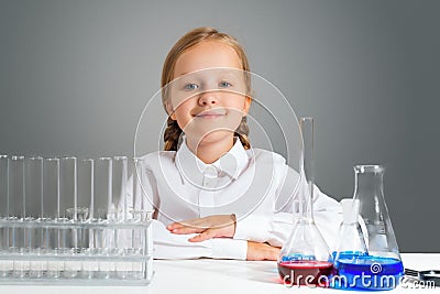 Little girl with flasks for chemistry sits at a table and looks at the camera Stock Photo
