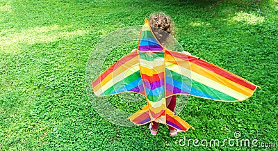 Little girl flies a rainbow kite. Child stands on the green grass with colored kite. Concept of innovation, ecology and outdoor Stock Photo