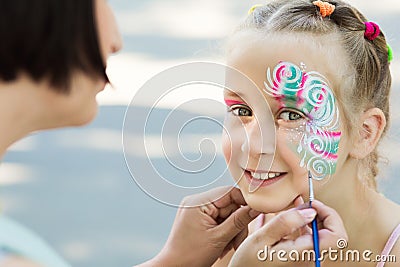 Little girl getting her face painted by face painting artist. Stock Photo