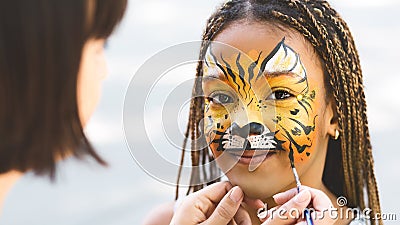 Little girl getting her face painted by face painting artist. Stock Photo