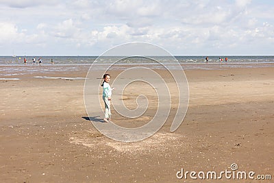 A little girl with glasses is flying her wind kite standing on a sandy beach Stock Photo
