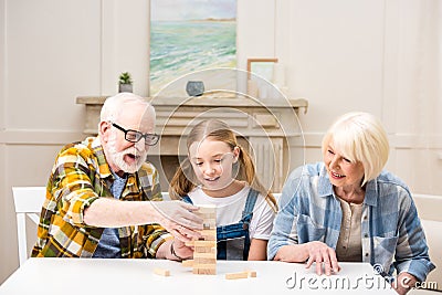 Little girl with grandfather and grandmother playing jenga game at home Stock Photo