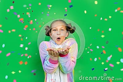 A little girl on a green isolated background in a bright suit blows away a streamer. Space for text. The concept of a holiday, Stock Photo