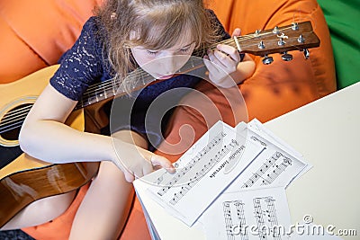 A little girl learns to play the guitar by sheet music Stock Photo