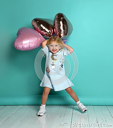 Little girl has fun with a bunch of pink air balloons in the shape of her heart. Stock Photo