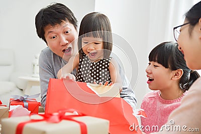 Little girl with her family unwrapping a red gift box. Stock Photo