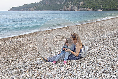 A little girl with her mother looks at the pebbles on the shore Stock Photo
