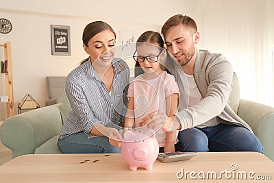 Little girl with her parents putting coins piggy into bank indoors. Money savings concept Stock Photo