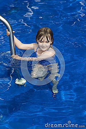 Little girl holding unto railing to step into deep blue pool Stock Photo