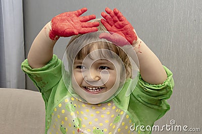 A little girl holds her hands above her head, which are smeared with children`s hand paints. Concept: development of creativity an Stock Photo