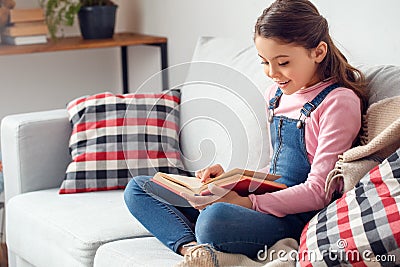 Little girl at home sitting reading book excited Stock Photo