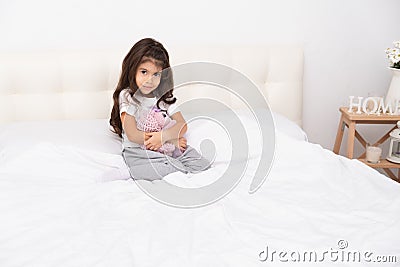 Little girl in home wear sits with teddy bunny on bed at home Stock Photo