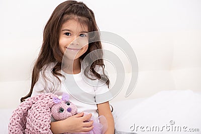 Little girl in home wear sits with teddy bunny on bed at home Stock Photo