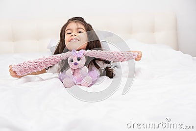 Little girl in home wear sits with teddy bunny on bed at home Stock Photo