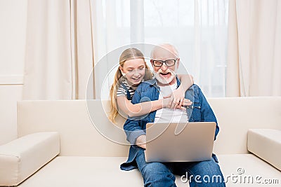 Little girl hugging happy grandfather using laptop at home Stock Photo