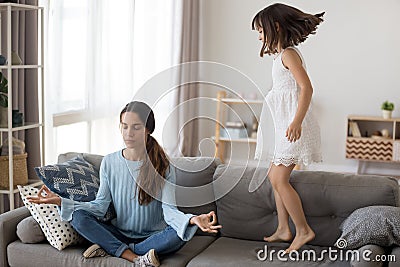 Little girl jumps on couch mother doing yoga Stock Photo