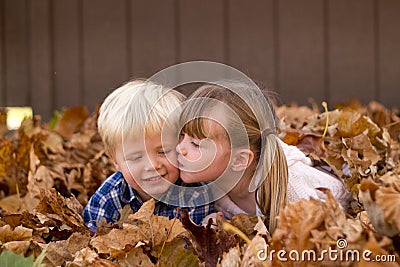 Little girl kissing a little boy laying in leaf pile leaves Stock Photo