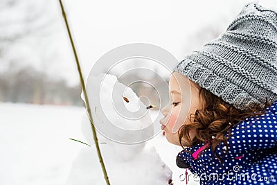 Little girl kissing a snowman in winter nature Stock Photo