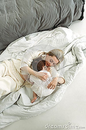 The little girl lay down on her mother and wants to sleep. Mom tenderly hugs her daughter Stock Photo