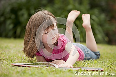Little girl laying in grass reading Stock Photo
