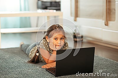 A little girl lies on the carpet in front of a computer screen. Online communication Stock Photo