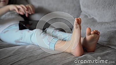 A Little Girl Lies at Home on the Couch and Looks into the Black Tablet. the Child Plays and Watches the Video Stock Footage - Video of phone, press: 215211398 