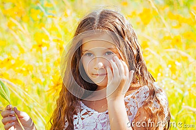 Little girl with long hair in a white dress rejoices in a field with flowers Stock Photo
