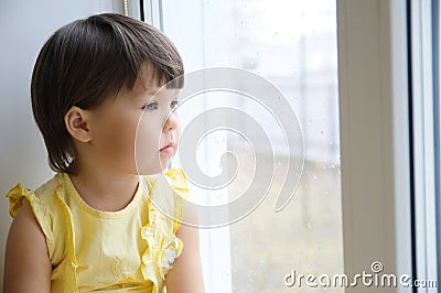 Little girl looking out the window longing for some sunshine. child sitting home at rainy day Stock Photo