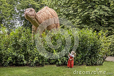 Little girl looking up at a big dinosaur, Girl in red dress, Brontosaurus dinosaur behind a big bush Editorial Stock Photo