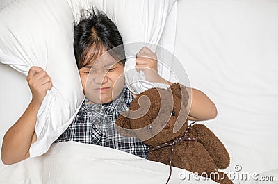 Little girl lying in bed covering head with pillow because too loud annoying noise Stock Photo