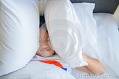 Little girl lying in bed covering head with pillow because too loud annoying noise Stock Photo