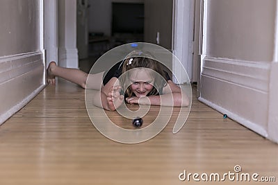 Little girl lying on corridor hardwood floor playing with small and large glass marbles Stock Photo