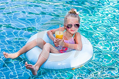 Little girl lying on inflatable ring in swimming pool. In the hands of a glass of mango juice. Holidays. Stock Photo