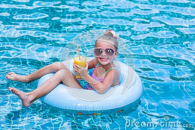 Little girl lying on inflatable ring in swimming pool. In the hands of a glass of mango juice. Holidays. Stock Photo