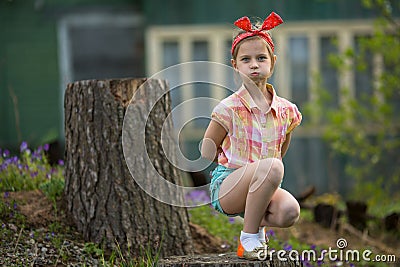 Little girl makes faces at the camera while sitting near country house. Stock Photo